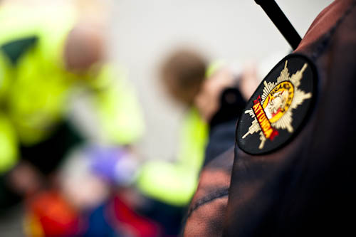 Närbild av ett märke på brandmans uniform och sjukvårdspersonal i bakgrunden Närbild av ett märke på brandmans uniform och sjukvårdspersonal i bakgrunden